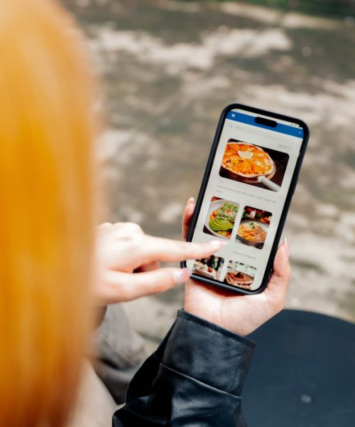 Two people browsing a food delivery app on a smartphone in an urban setting. Ideal for concepts of mobile technology, lifestyle, and modern dining solutions.